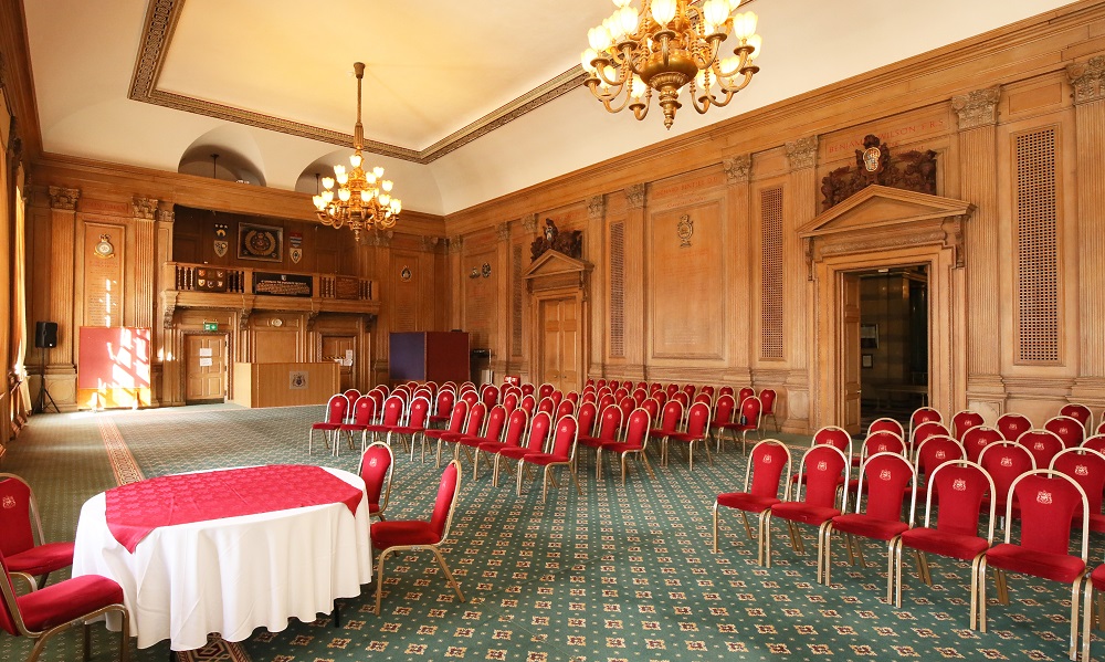 A view of the Banqueting Hall at Leeds Civic Hall set up for a wedding ceremony. The view is from the side of the room, the walls of the room are clad in ornate wooden panelling and two large chandelliers hang from the ceiling