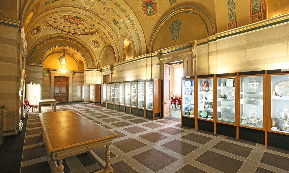 Entrance hall way to the Banqueting Room at Leeds Civic Hall. There are glass cabinets lining the walls containing trophys, plates and other artifacts.