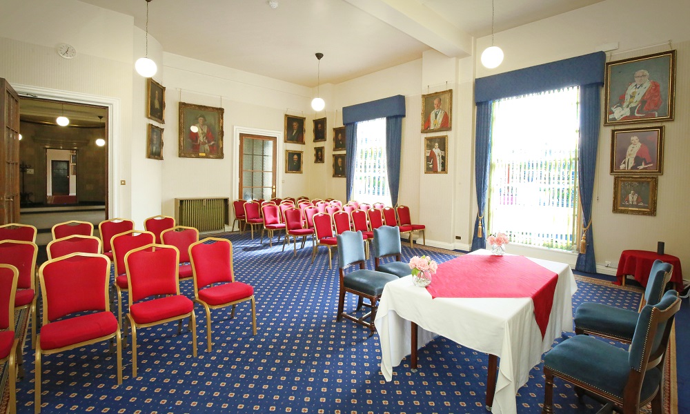A view of the west room at Leeds Civic Hall from the front right corner of the room looking towards the entrance door. The walls have historic portraits on them.