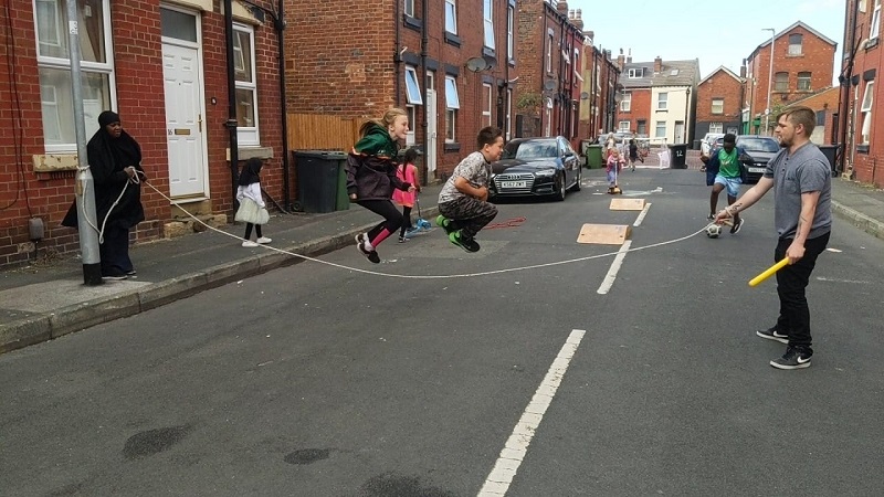 children playing with a long skipping rope on a closed residential street