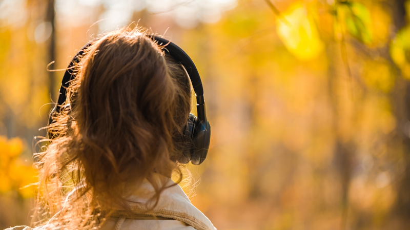 person with long wavy hair that is tied back wearing headphones and walking in nature