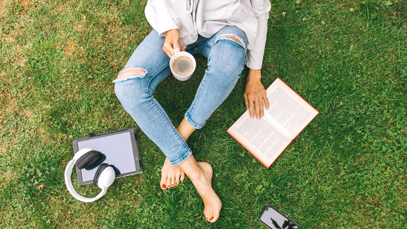 person sat on grass relaxing and reading with a drink