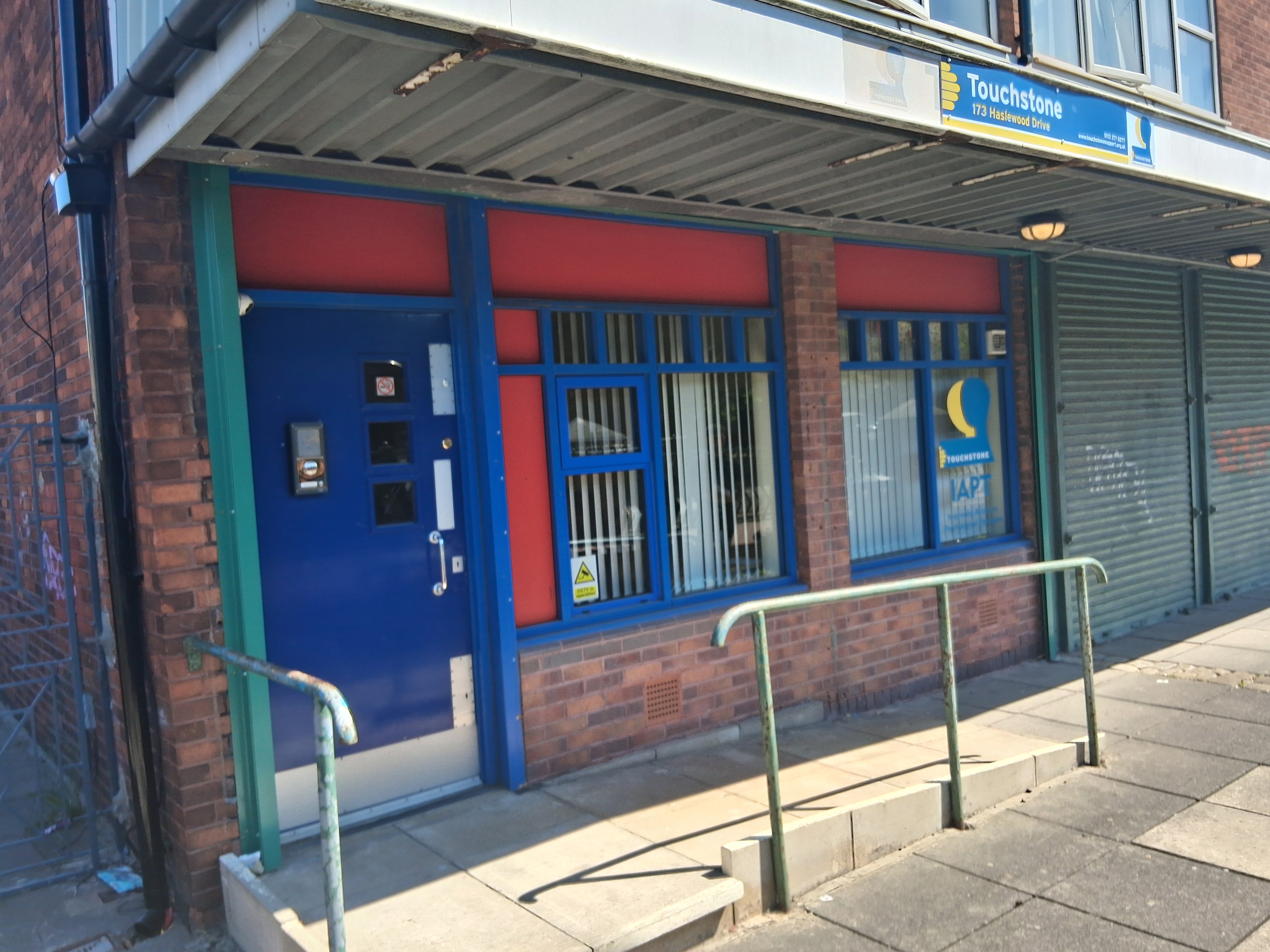 Front of groundfloor premises with two windows and paving with guardrail leading to door