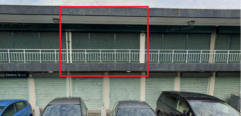Two floors of shuttered commercial units with car park in front and one of the upstairs units highlighted in red