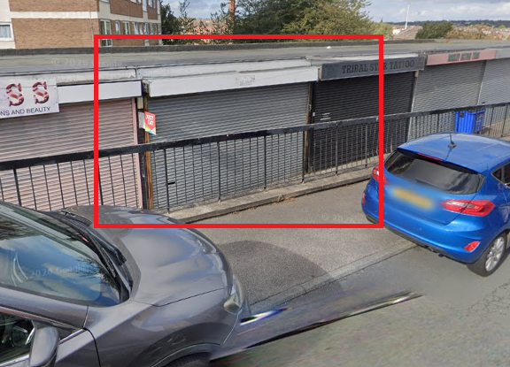 Row of shuttered shop premises, separated from road by metal railings