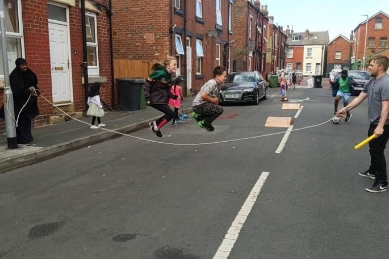 Children playing with a long skipping rope on a closed residential street