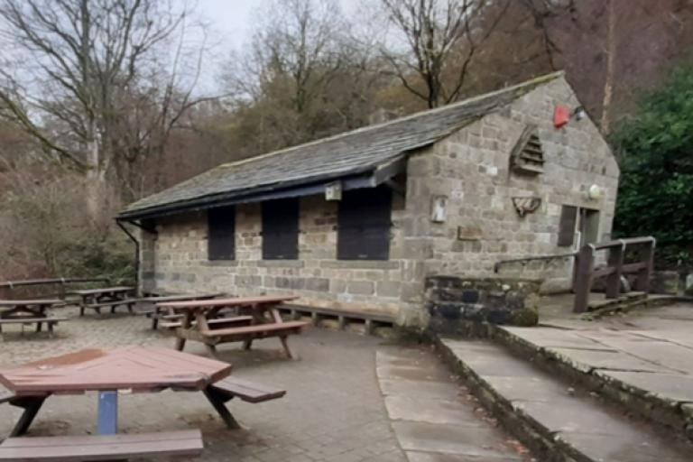 One storey stone building with wooden tables outside, situated in front of a wood