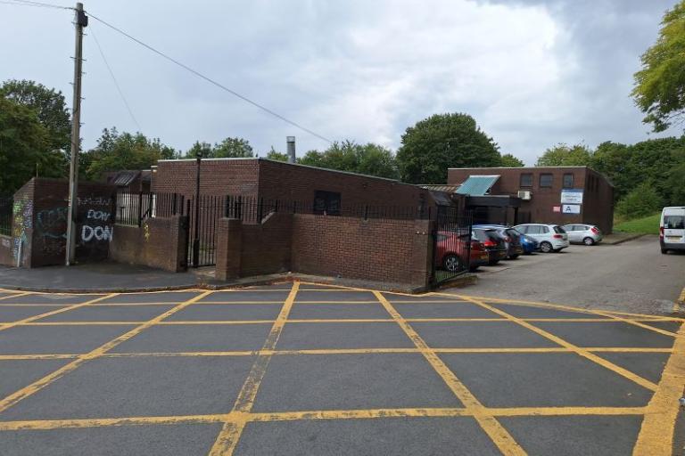 Photograph showing the exterior of single storey building at Strawberry Lane with parking spaces to front and trees at rear