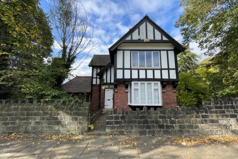 View of Abbey Lodge, a three-storey Tudor-style property, with trees to either side and pavement in front