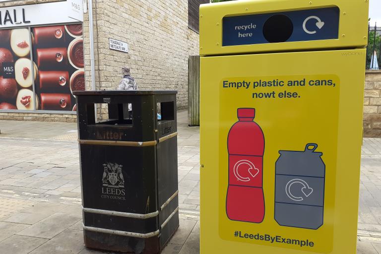Image shows yellow recycling on-the-go bin next to a black bin on a high street