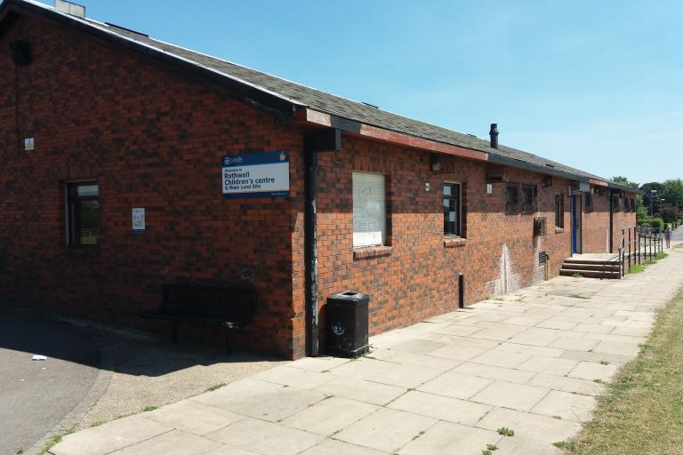 Image shows single storey redbrick building with sloping roof, alongside concrete path