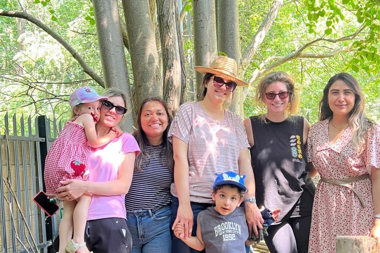 Image shows group of smiling women and children standing outside under trees