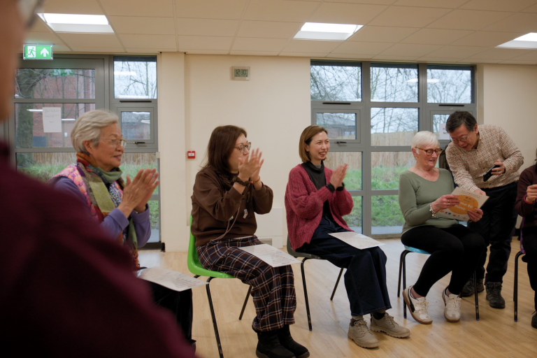 Image shows row of seated adults in an indoor space, smiling and clapping
