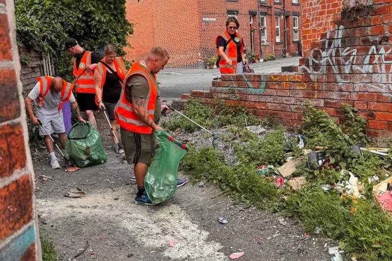 Image shows group of adults picking litter on a redbrick terrace street
