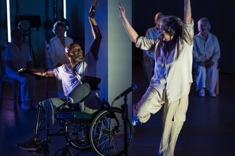 Image shows man in a wheelchair dancing in a performance alongside a standing dancing woman