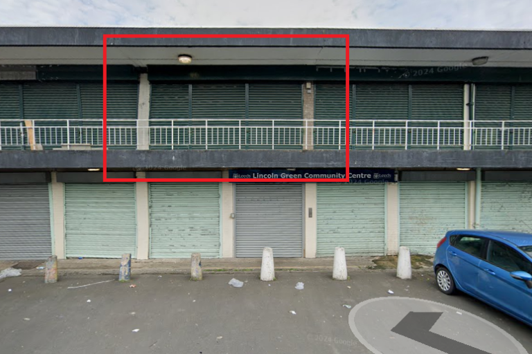 Two floors of shuttered commercial units with car park in front and one of the upstairs units highlighted in red